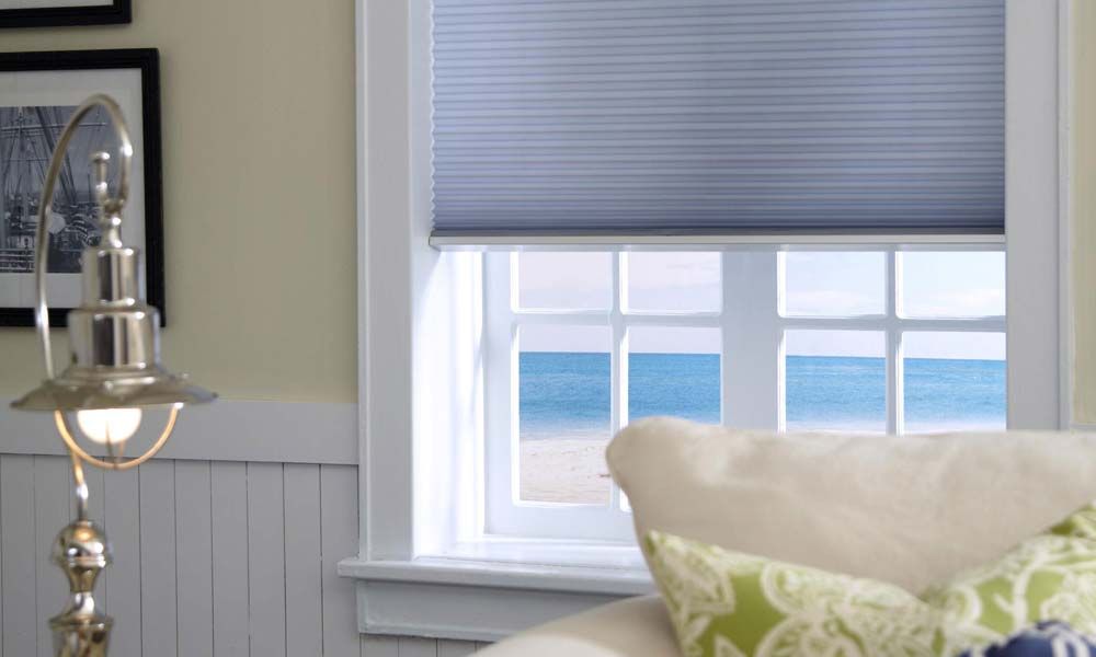 blue honeycomb shades on a window overlooking the ocean